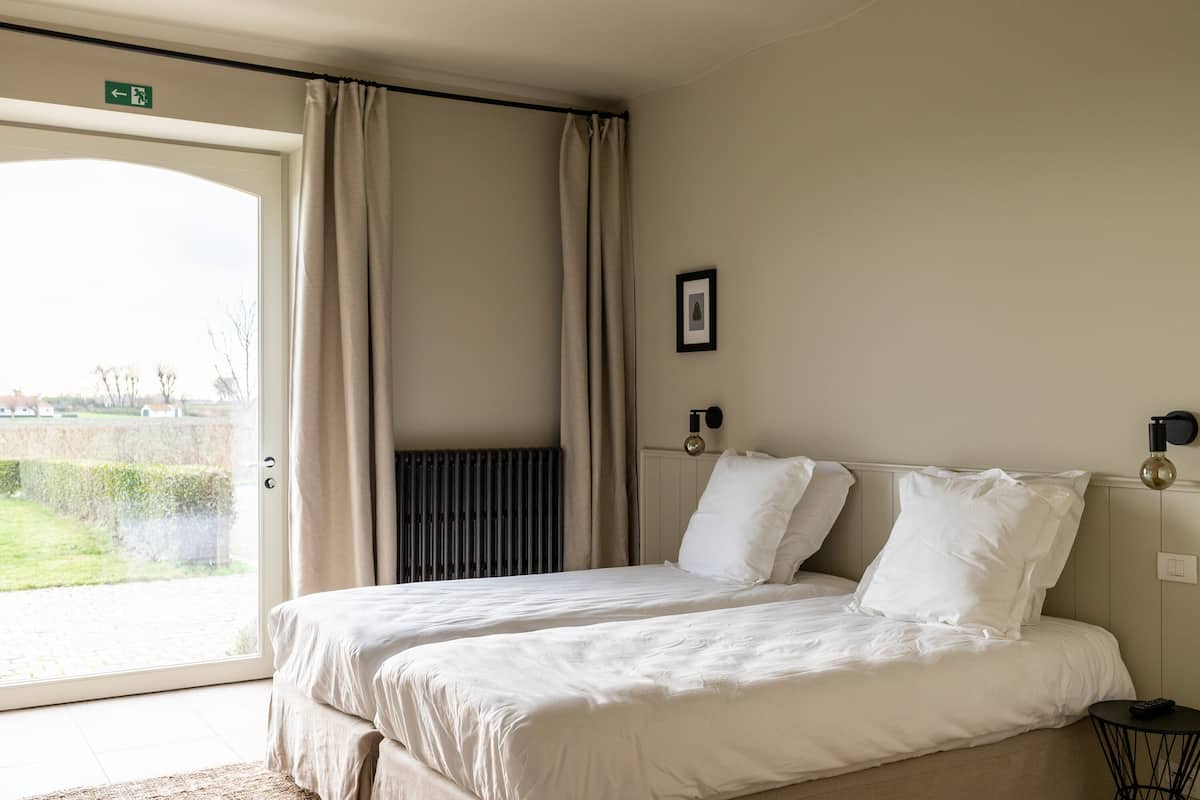 A hotel room with a bed, a radiator, a picture on the wall, and a view of the outside.