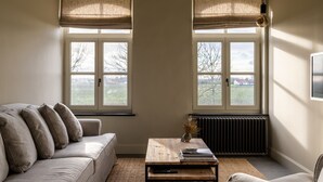 Ein Wohnzimmer mit einer Couch, einem Couchtisch und zwei Fenstern mit Jalousien.