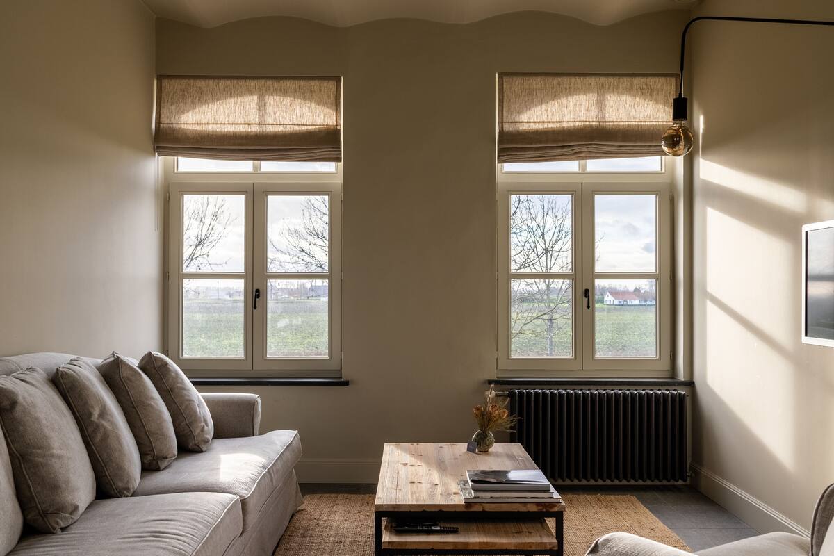 A living room with a sofa, a coffee table, and two windows with blinds.
