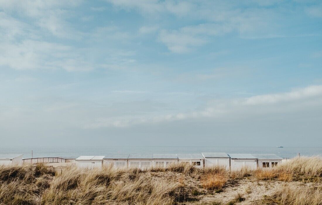 Una hilera de cabañas blancas en la playa, con arena al frente y cielo despejado.