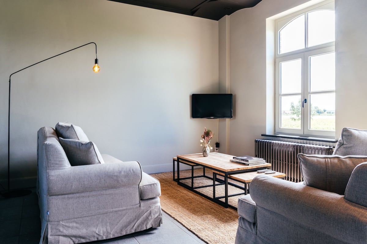 A modern living room with two grey sofas, a wooden coffee table, a floor lamp, and a TV mounted on the wall.