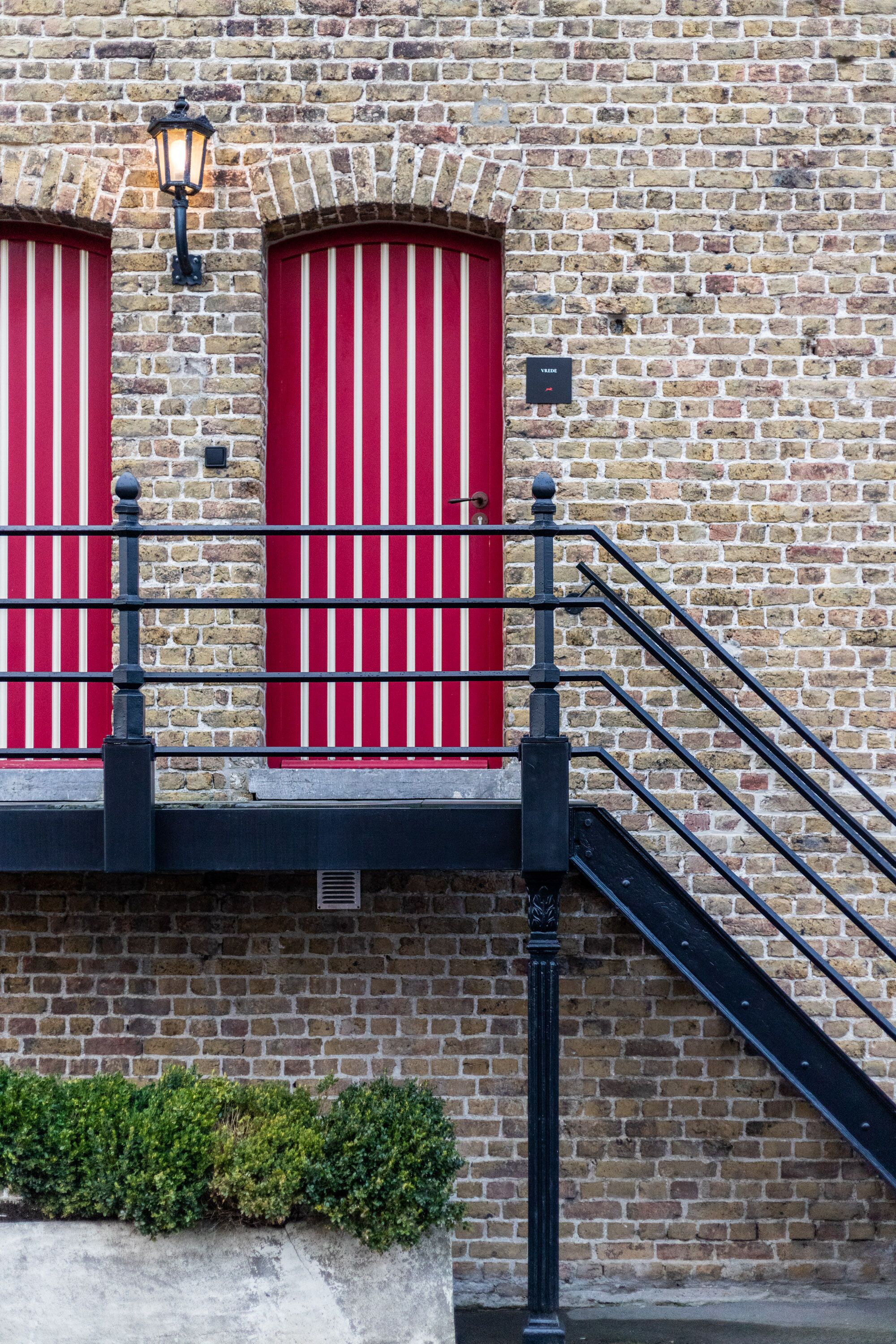 A brick building with red-framed windows and a black metal staircase.