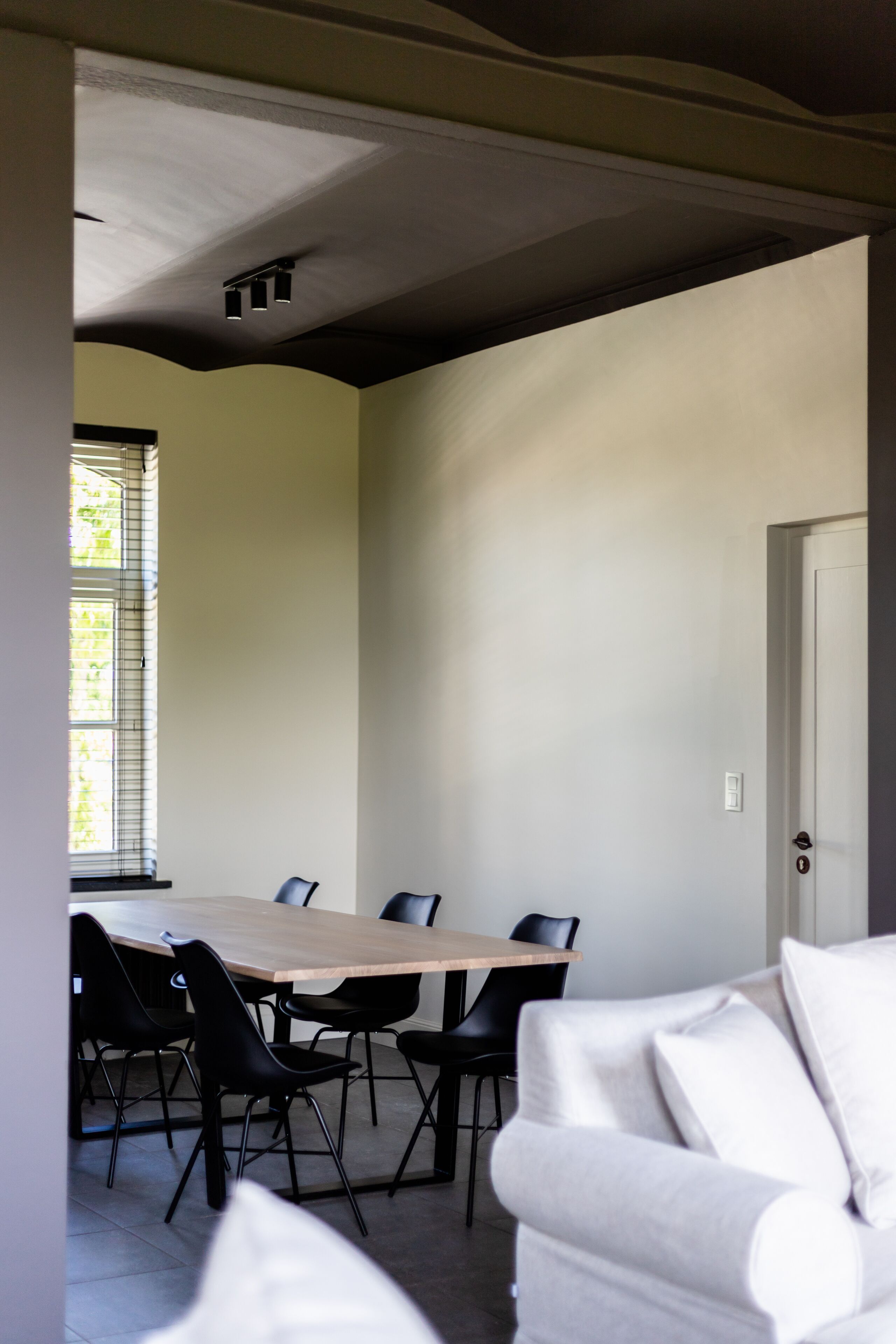 Un coin repas avec une table en bois et des chaises noires, un canapé blanc et une porte.