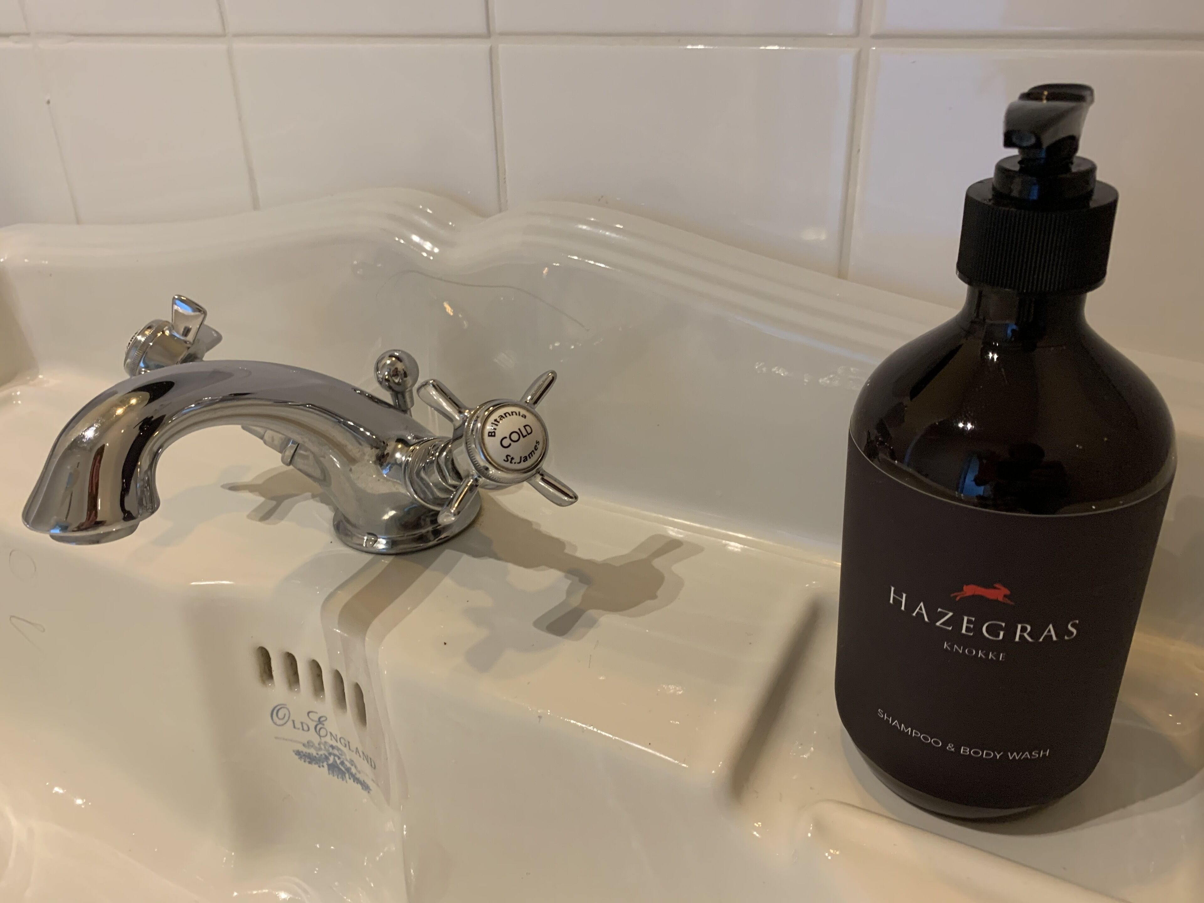 A bathroom sink with a faucet and a bottle of Hazegras shampoo.