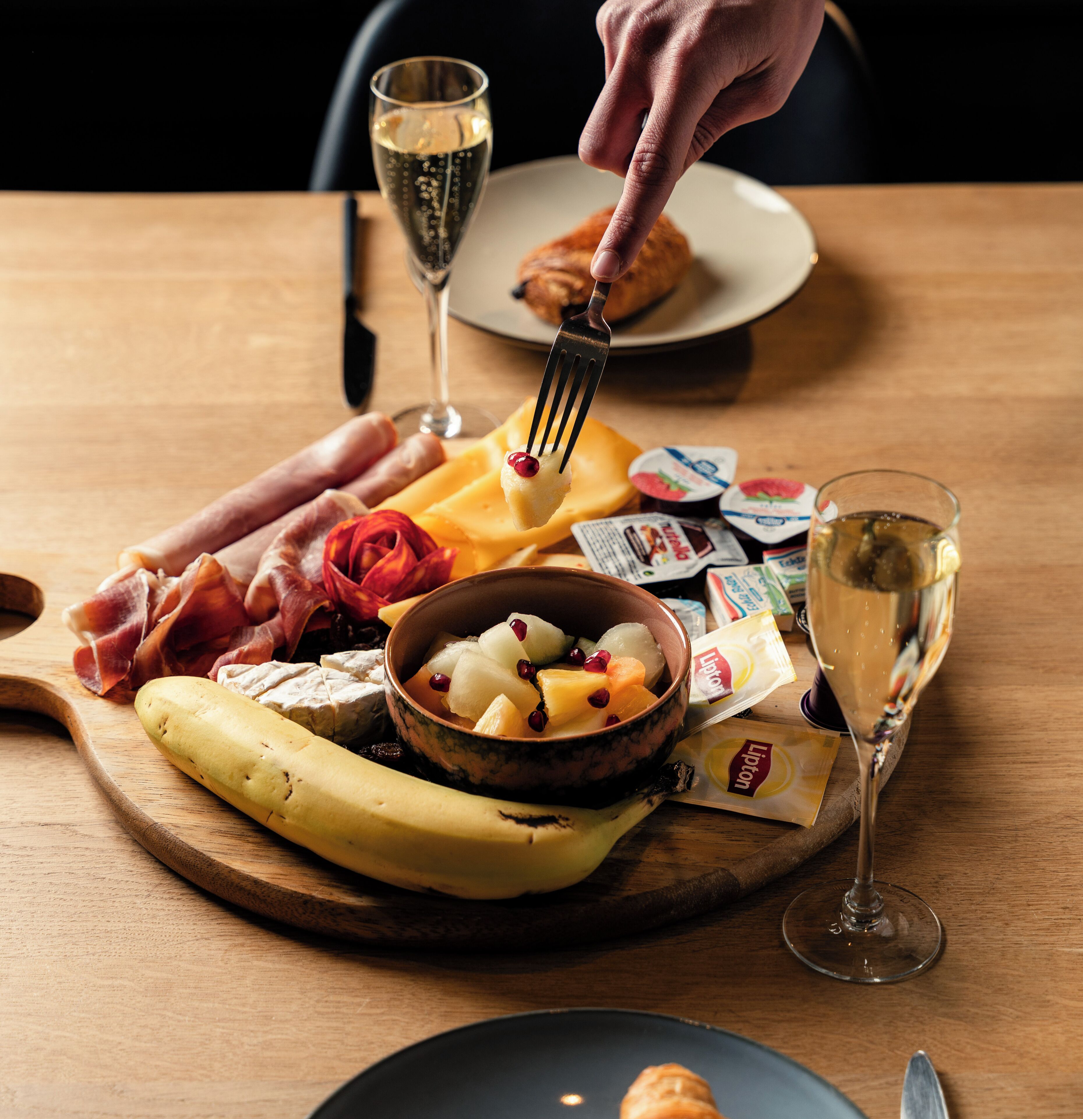 Een houten tafel met een kaasplank, fruit en een fles Lipton thee.