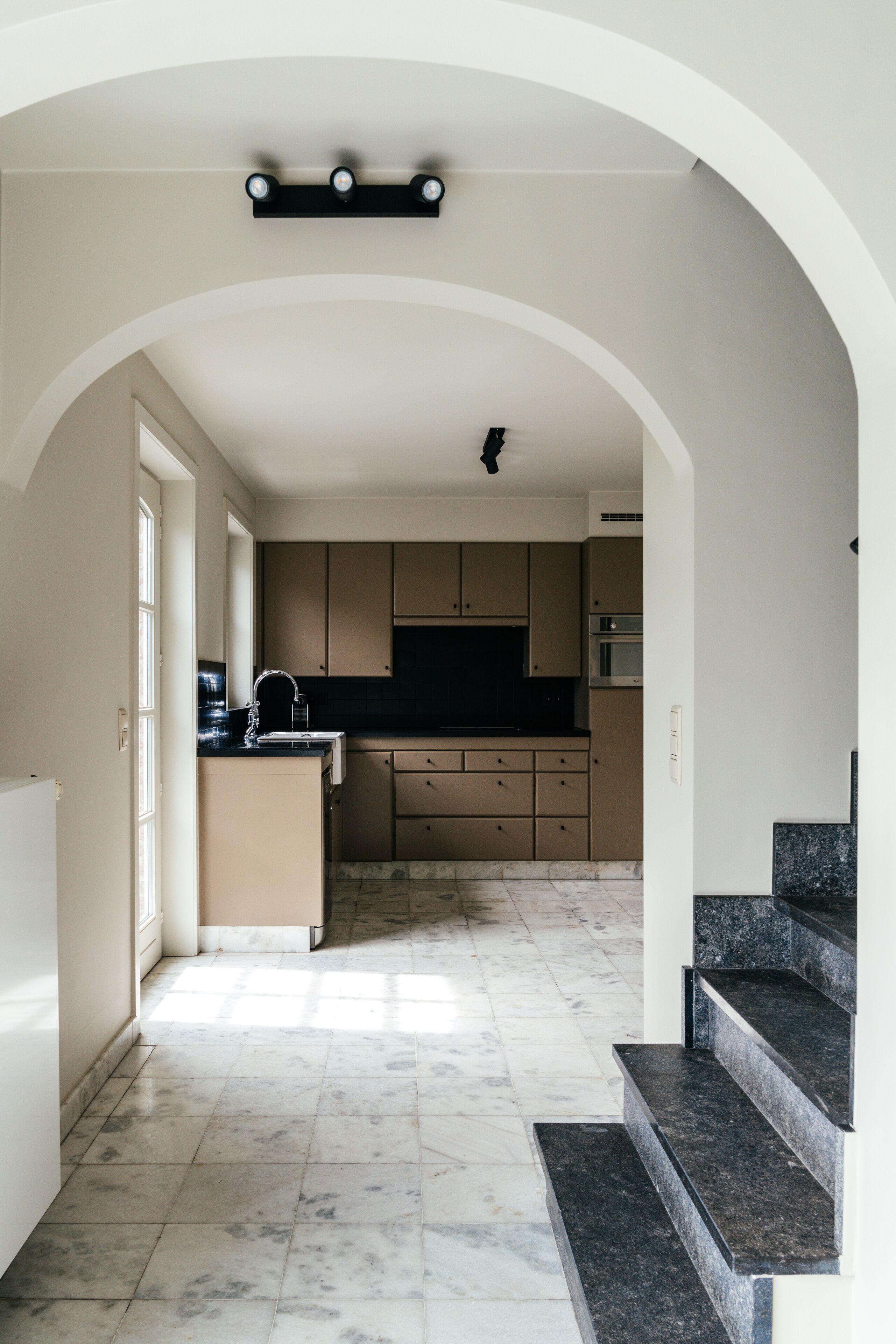 Une cuisine moderne avec un sol en marbre, un plan de travail noir et des armoires de couleur beige.