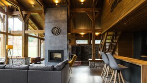 A modern interior with a stone fireplace, wooden beams, and a bar area with stools. - Chalet for up to 10 people with sauna nestled in the valley of 3 mountains (Razlog)