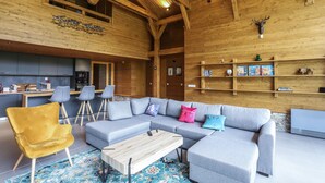 A spacious living area with a large grey sectional sofa, a yellow armchair, and a wooden coffee table. There are multiple grey chairs and a small kitchen area in the background. - Chalet for up to 10 people with sauna nestled in the valley of 3 mountains (Razlog)