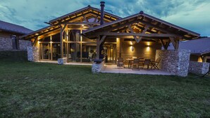 A modern house with a stone exterior, large glass windows, and a wooden deck with outdoor seating. - Chalet for up to 10 people with sauna nestled in the valley of 3 mountains (Razlog)