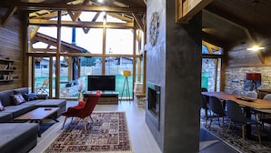 A spacious living area with a large window, a fireplace, a dining table, and a sofa. - Chalet for up to 10 people with sauna nestled in the valley of 3 mountains (Razlog)