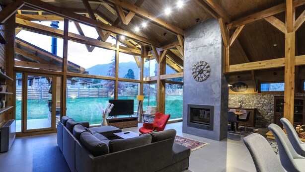 A spacious living room with a large window, a fireplace, and a cozy seating area. - Chalet for up to 10 people with sauna nestled in the valley of 3 mountains (Razlog)
