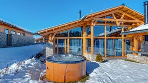 A wooden cabin with a glass-enclosed porch, stone walls, and a hot tub in the foreground. - Chalet for up to 10 people with sauna, private home theater and hot tub (Razlog)
