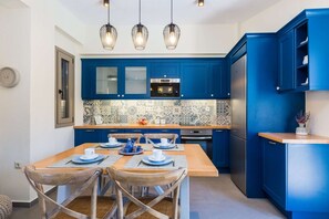 A modern kitchen with blue cabinets, a wooden dining table, and three pendant lights.