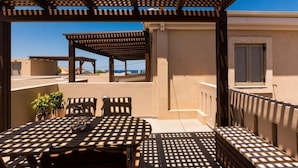Un espace extérieur aménagé, abrité et doté d’une table et de chaises, d’une pergola au-dessus et d’une vue sur la mer.