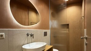 Un bagno moderno con un ampio specchio ovale, un lavabo bianco e un box doccia.