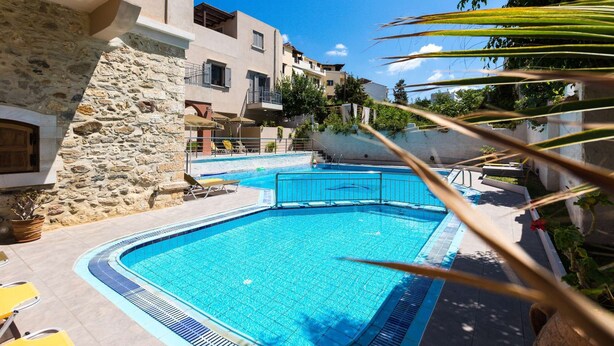 Ein Pool mit Liegestühlen und Sonnenschirmen, umgeben von Steinmauern und Gebäuden.