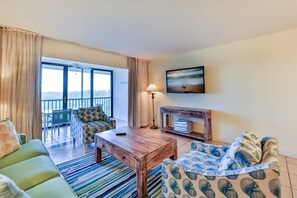 A living room with a sofa, a coffee table, a TV, a fireplace, and a balcony with a view. - SOUTH Villa 5310 - Three bedroom condo with Bay views (Captiva)