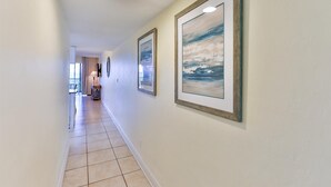 A hallway with framed artwork on the walls, a tiled floor, and a door at the end. - SOUTH Villa 5310 - Three bedroom condo with Bay views (Captiva)