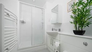 Un baño moderno con cabina de ducha de vidrio, un lavamanos blanco y una planta en maceta.