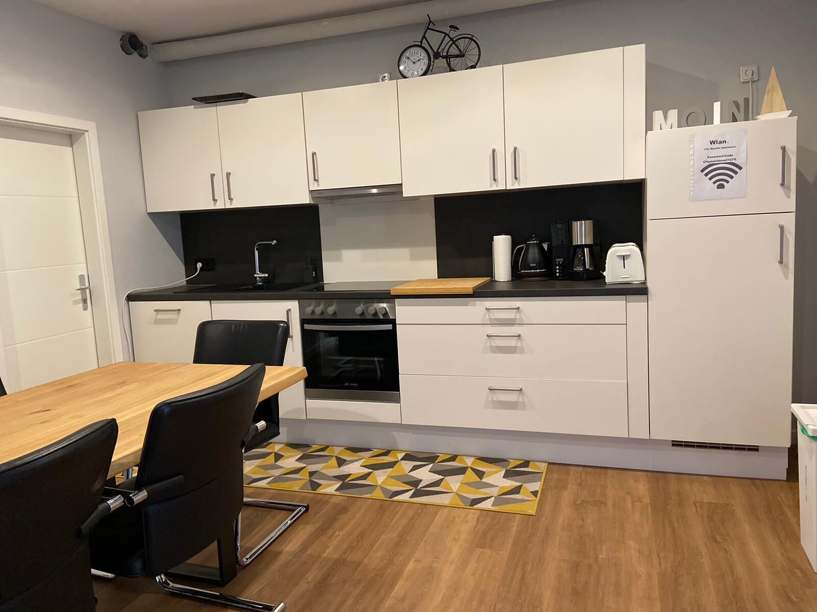 Eine kleine Küche mit weißen Schränken, einer schwarzen Arbeitsplatte, einem eingebauten Backofen und einer Kaffeemaschine.