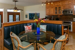 A modern kitchen with wooden cabinets, a built-in microwave, and a dining area with a glass table and leather booth seating.
