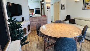 Ein modernes Wohnzimmer mit einem Holzesstisch, blauen Stühlen, einer kleinen Weihnachtstanne und einem Sofa.