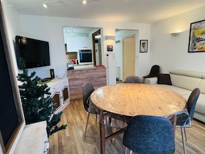 Ein modernes Wohnzimmer mit einem Holzesstisch, blauen Stühlen, einer kleinen Weihnachtstanne und einem Sofa.