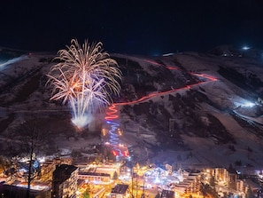 Un pueblo con montañas al fondo, edificios iluminados y un espectáculo de fuegos artificiales.