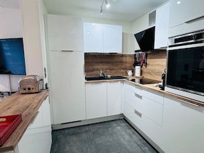 Una cocina moderna con armarios blancos, encimera de madera, horno empotrado y estufa negra.