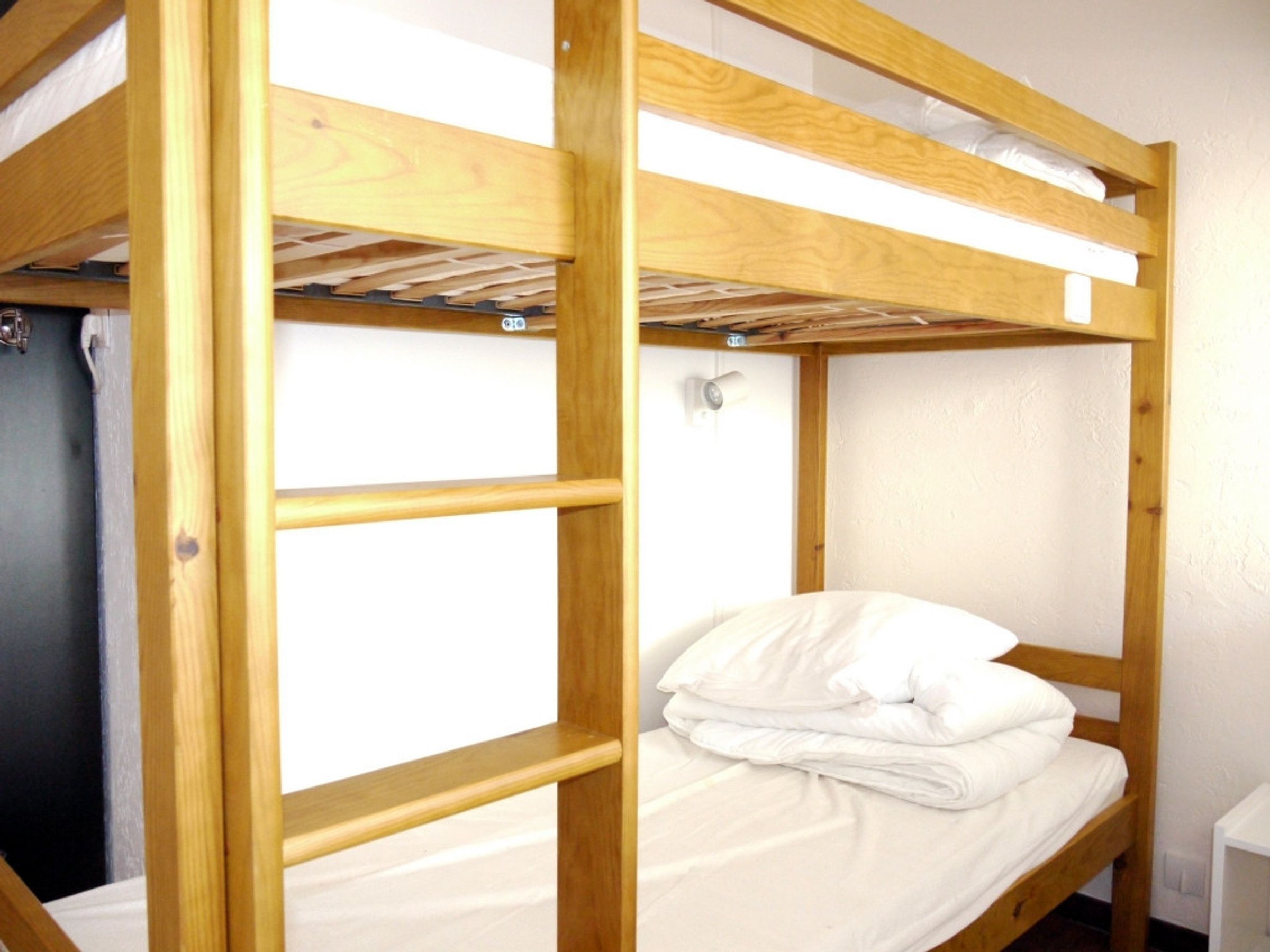 Un lit superposé avec une structure en bois et du linge de lit blanc.
