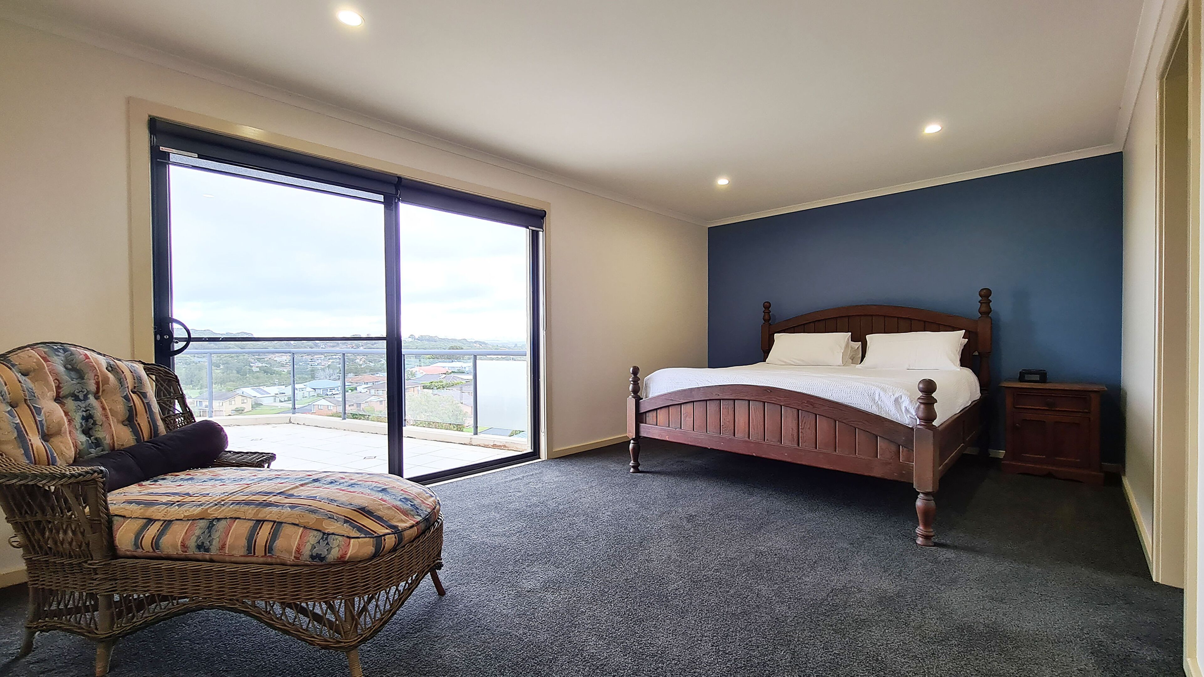 A bedroom with a bed, a chair, a nightstand, and a large window with a view.