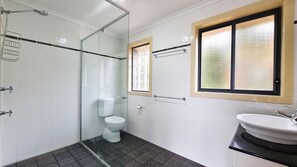 A bathroom with a glass shower enclosure, a toilet, a sink, and two windows. - A Vista, Townhouse 1 (Forster)