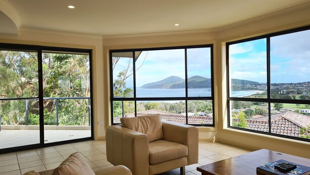 A spacious room with large windows offering a view of a coastal landscape and a mountain. - A Vista, Townhouse 1 (Forster)