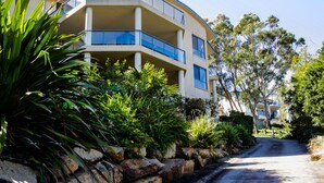 A multi-story building with balconies, surrounded by lush greenery and a paved driveway. - A Vista, Townhouse 1 (Forster)