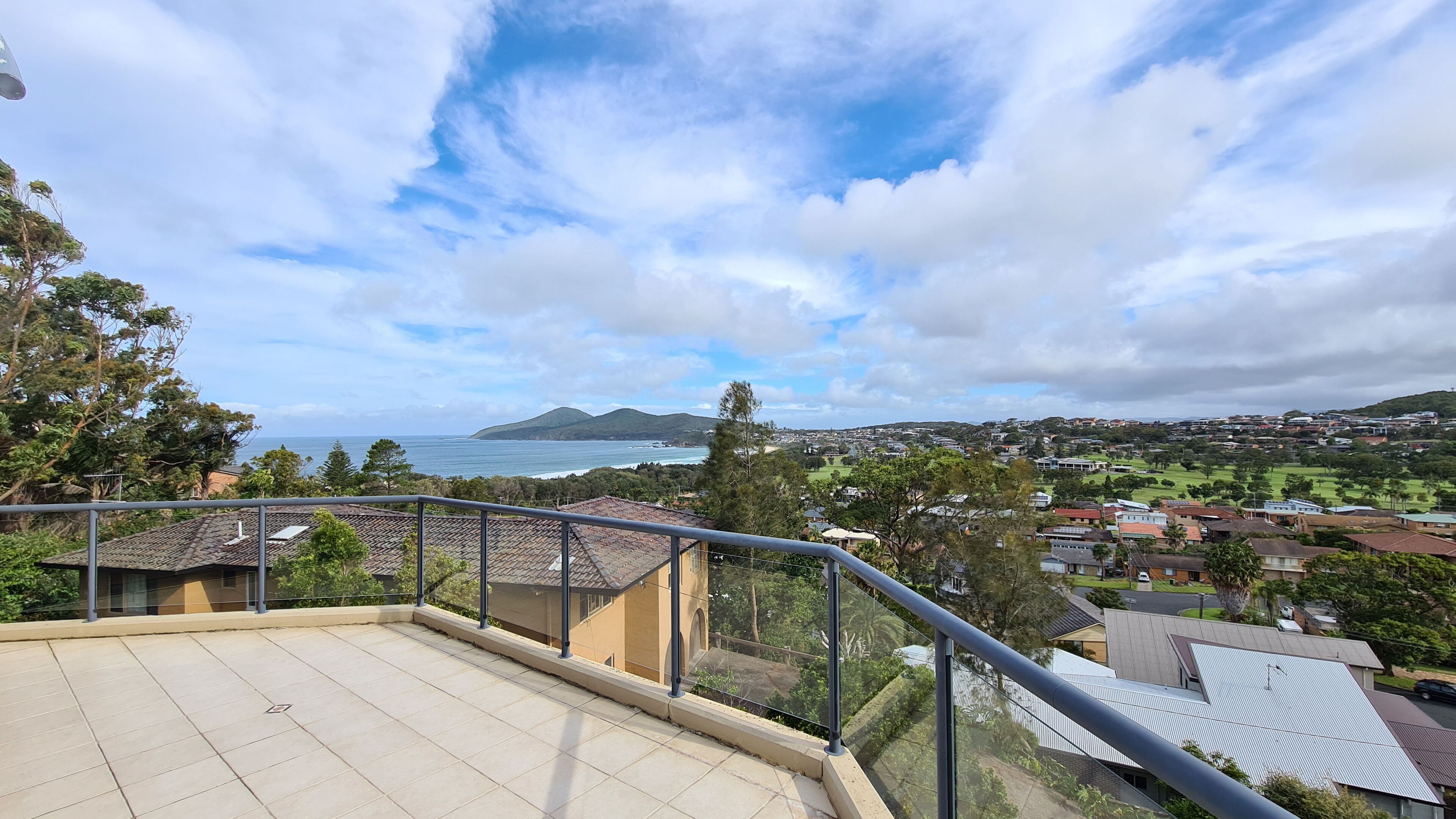 A balcony with a view of a coastal town, houses, and a mountain in the distance.