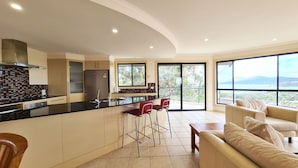 A modern kitchen with a central island, red bar stools, and a view of the outdoors through large windows. - A Vista, Townhouse 1 (Forster)