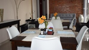 A dining area with a brick wall, a grey sofa, and a table set with white chairs. - Dei Gratia Guesthouse (Durban)