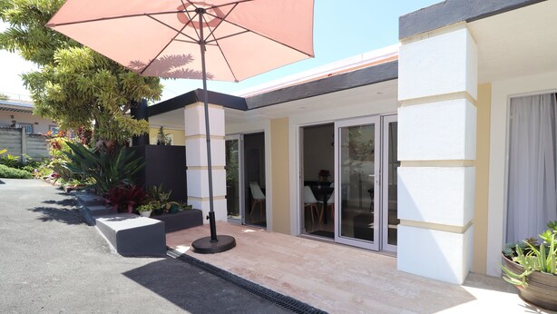A modern building with a covered patio area, large windows, and potted plants. - Dei Gratia Guesthouse (Durban)