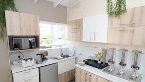 A modern kitchen with wooden cabinets, a built-in microwave, a coffee maker, and a sink. - Dei Gratia Guesthouse (Durban)