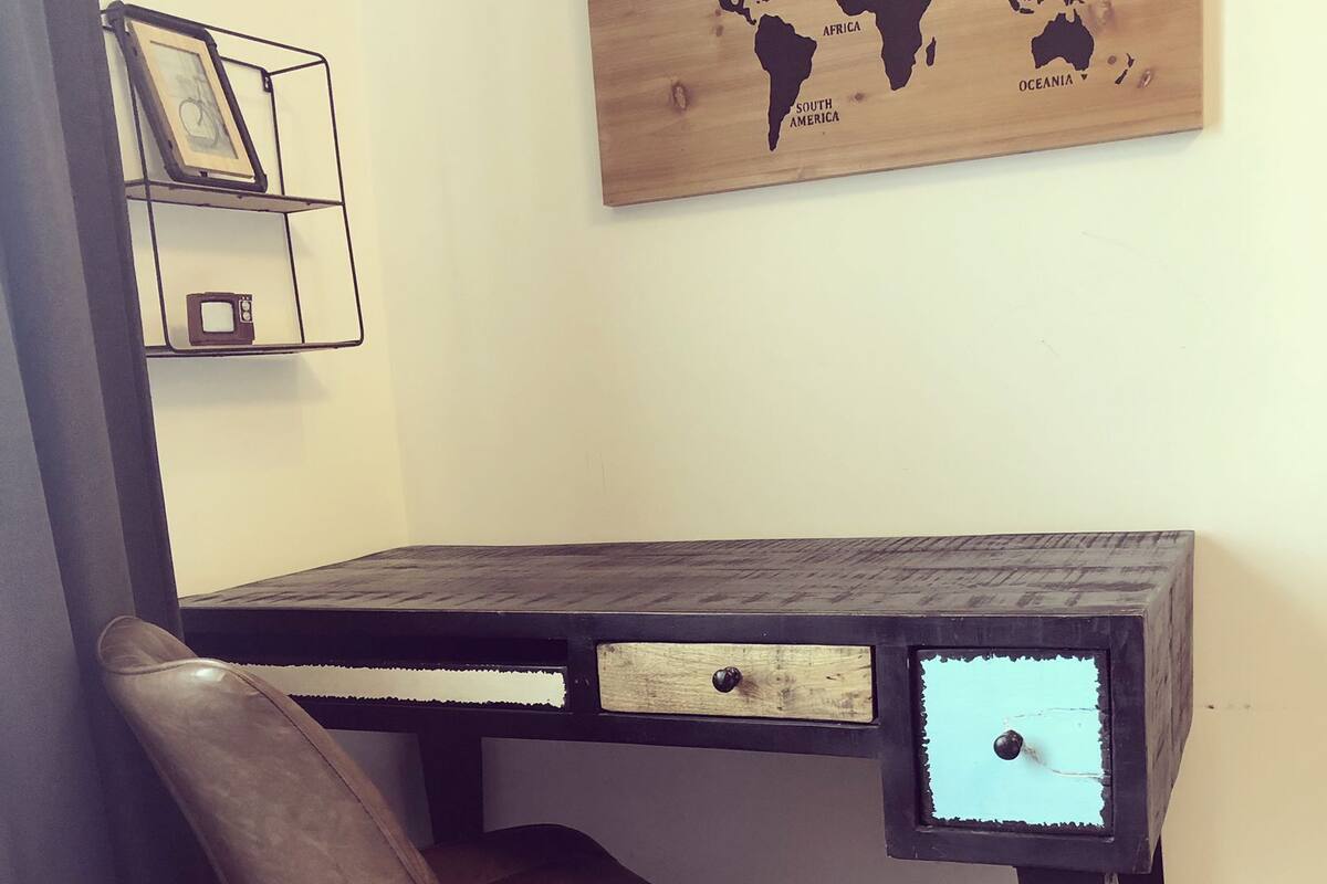 A wooden desk with a world map, a chair, and a small shelf with a picture frame and a clock.