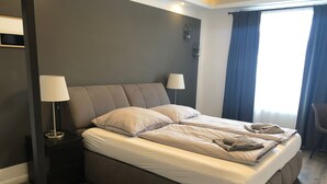 Una habitación de hotel moderna con una cama grande, dos lámparas de noche, una pared oscura y una ventana con cortinas.
