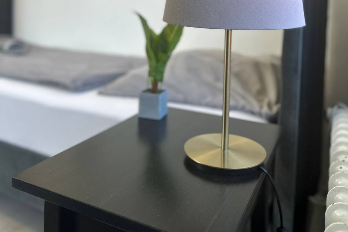 A modern bedroom with a bedside table, a lamp, a small plant, and a bed.