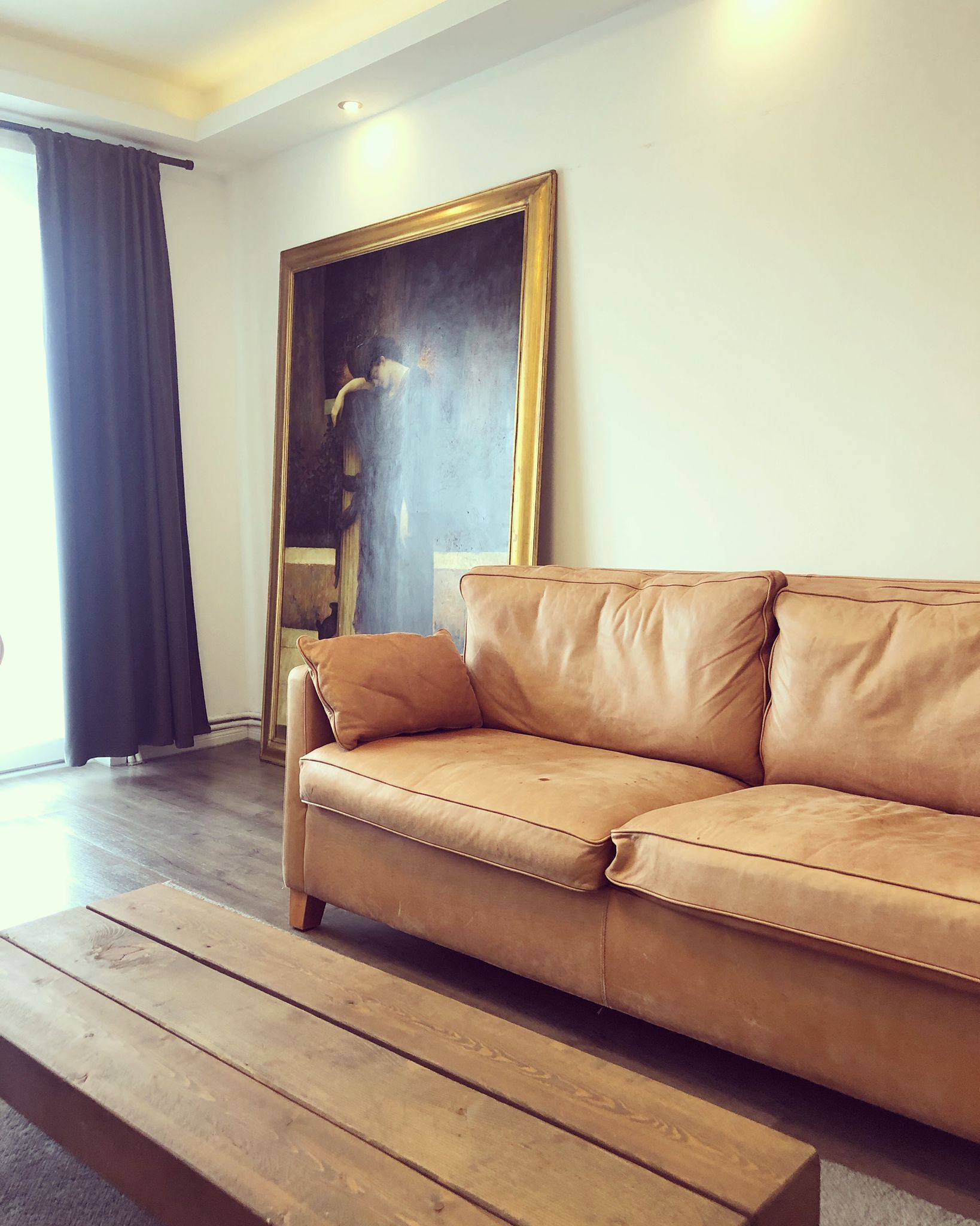 A living room with a brown leather sofa, a wooden coffee table, and a large framed painting on the wall.
