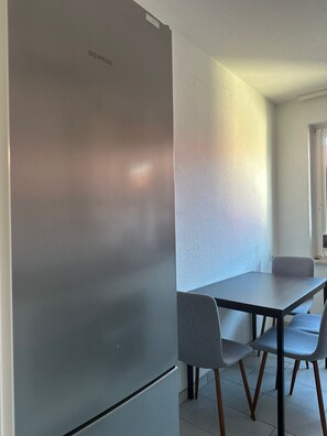 Una cocina moderna con un refrigerador de acero inoxidable, una mesa de comedor con cuatro sillas y un ventanal que proporciona luz natural.