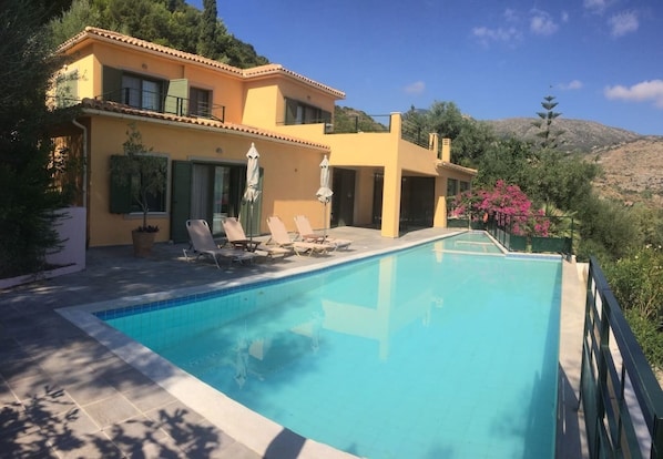 A poolside area with lounge chairs and a clear blue pool, surrounded by a yellow building with a balcony.