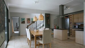 A modern kitchen with a dining area, featuring a wooden table, chairs, and pendant lights. - Lovely Open Plan Family Villa in Kato Katelios (Kefalonia)