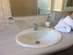 A bathroom with a white sink, a mirror, a towel, and a soap dispenser.