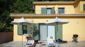A yellow building with a pool, two lounge chairs, and two umbrellas. - Lovely Open Plan Family Villa in Kato Katelios (Kefalonia)