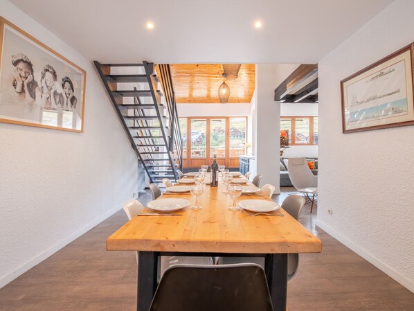 A dining area with a long wooden table set for a meal, a staircase, and framed pictures on the walls. - Spacious duplex in Les Deux Alpes, 10 pers, large terrace (Les Deux Alpes)
