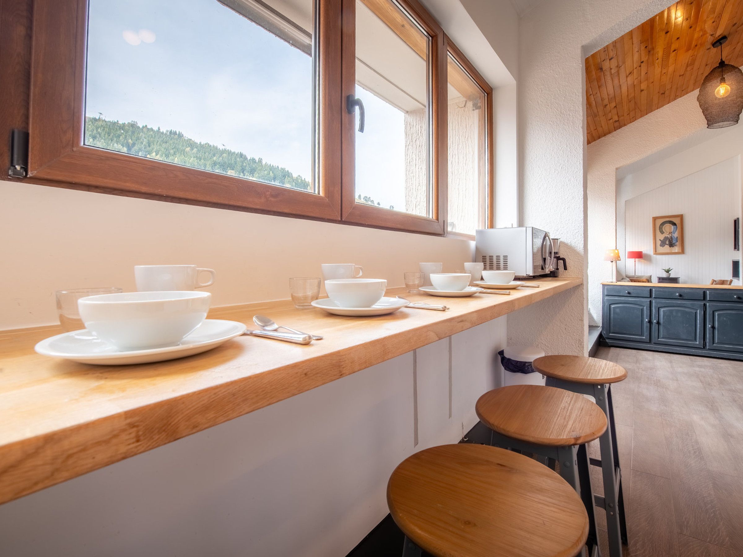 A kitchen with a wooden countertop, white cabinets, and a view of the outdoors through large windows.